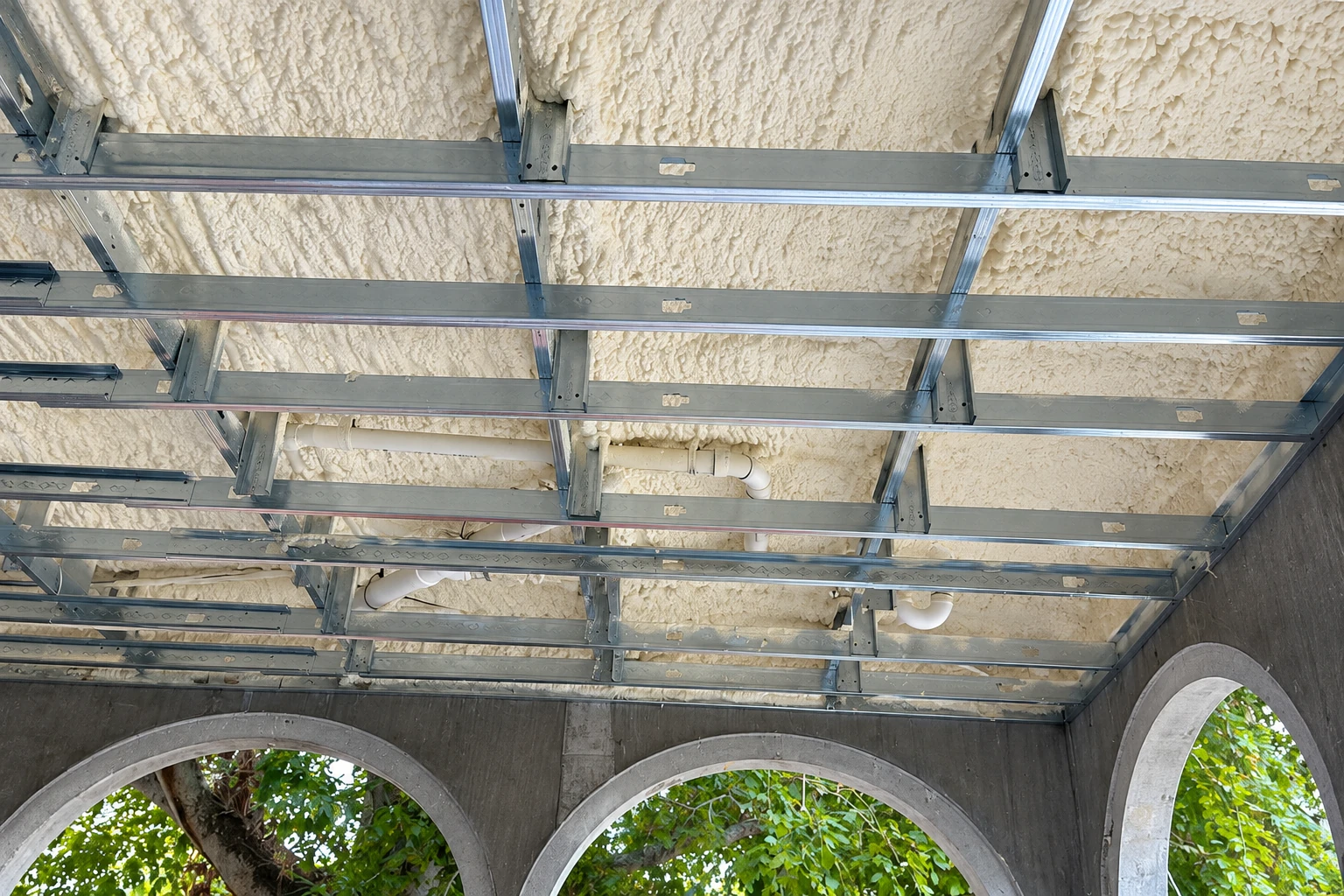 Ceiling framing coated with white spray foam insulation above concrete arches.