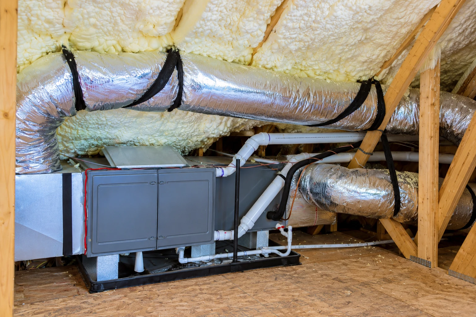 Attic HVAC system sits beneath exposed rafters, surrounded by spray foam insulation and foil-wrapped ducts.