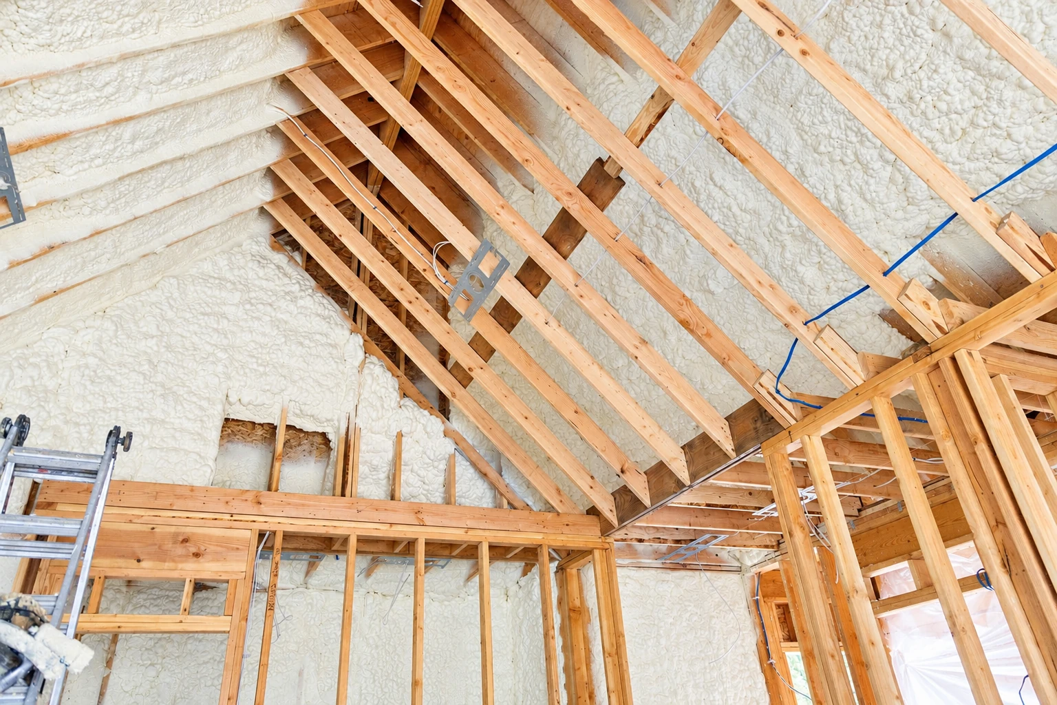 Open-cell spray foam insulation coats the roof and walls between exposed wooden rafters.
