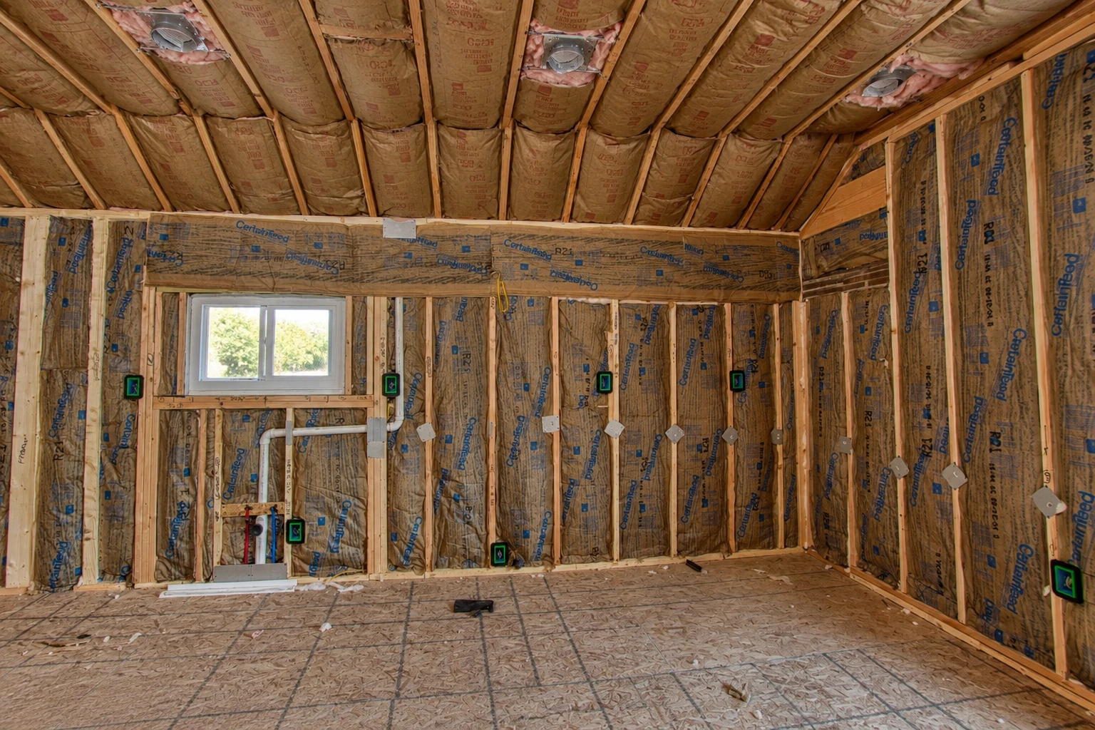 Unfinished room with fiberglass batts installed between wall studs and ceiling joists.